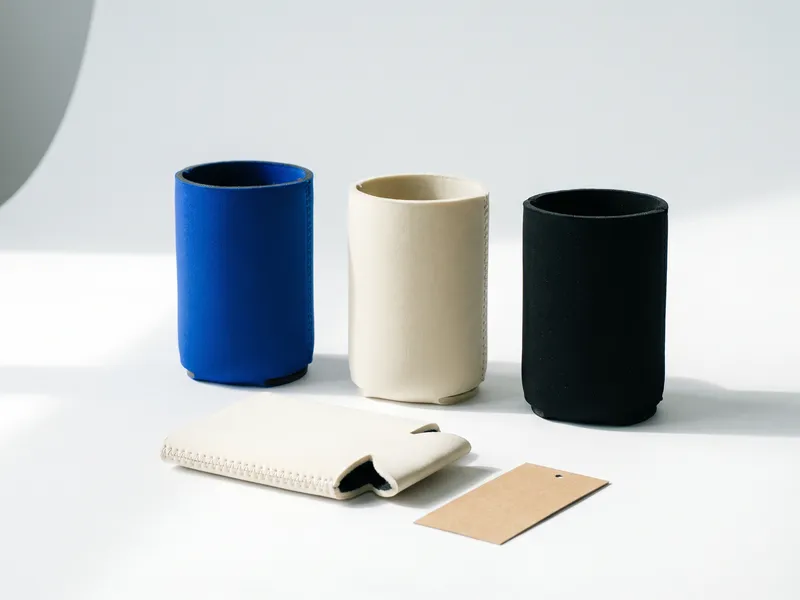 Three neoprene custom koozies in cobalt, cream and black standing in a row