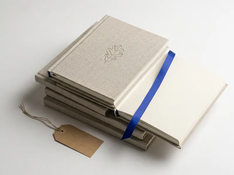 Stack of linen custom notebooks with debossed emblem and cobalt ribbon